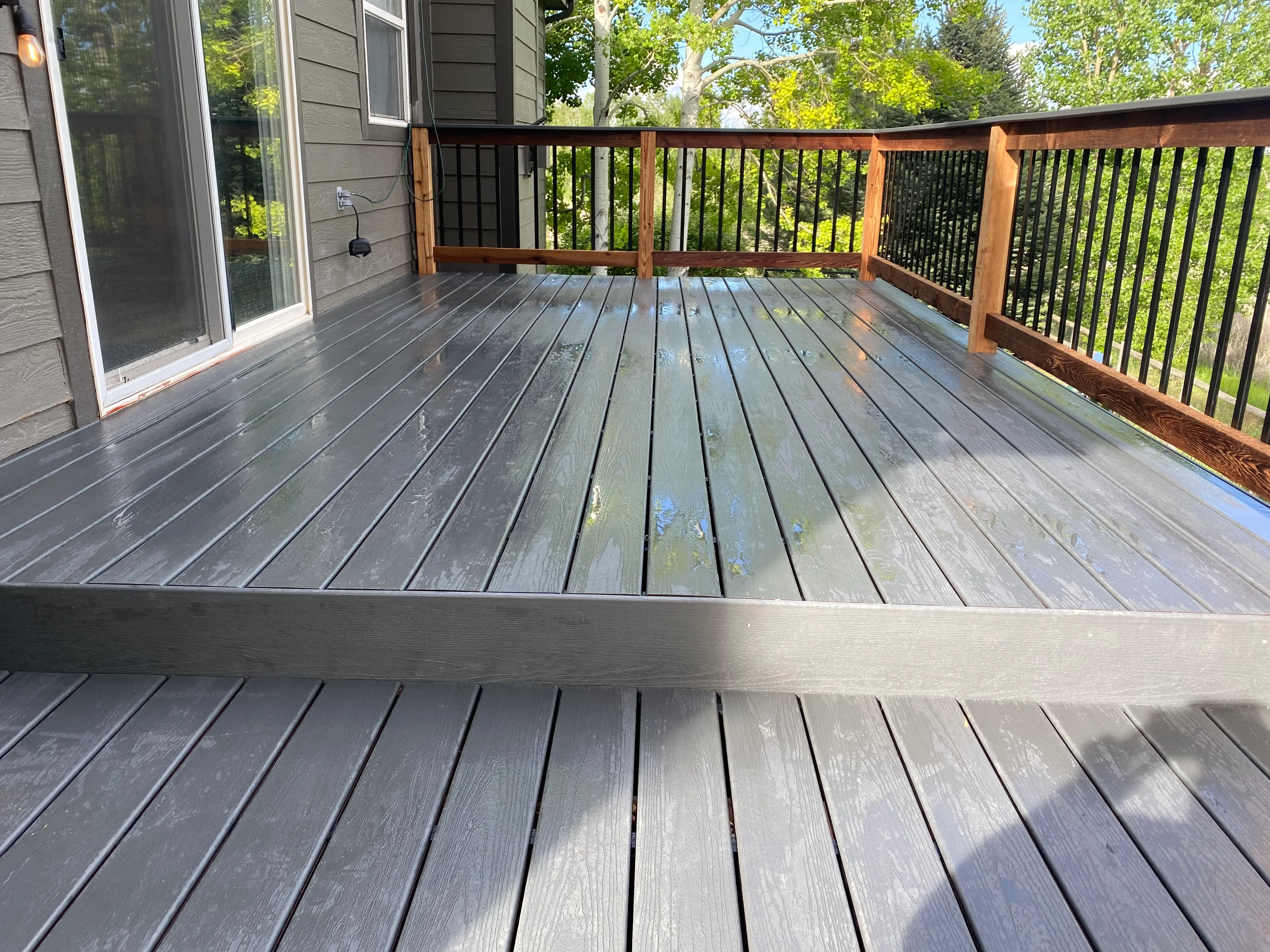 Gray composite deck with two levels, wood posts, and black metal railings overlooking green landscape